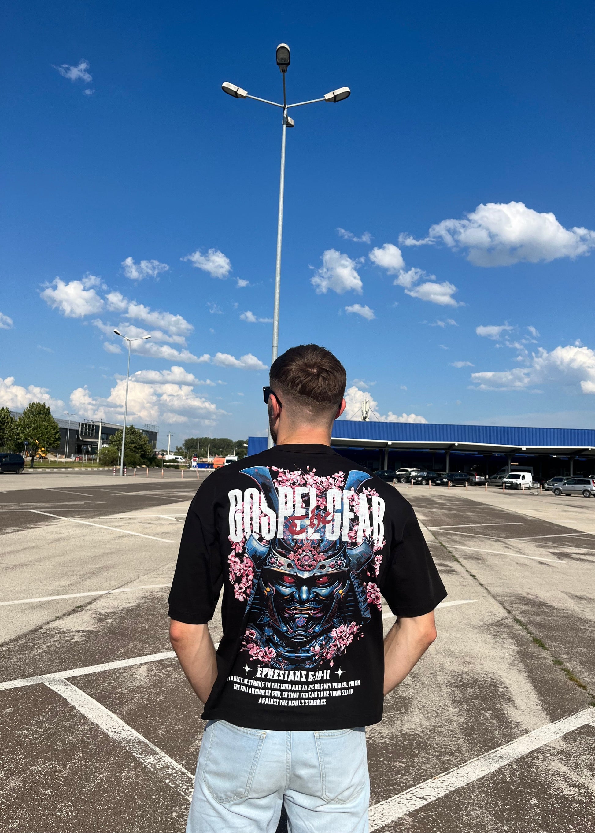 Person wearing a graphic t-shirt standing on a road with a blue sky and clouds in the background